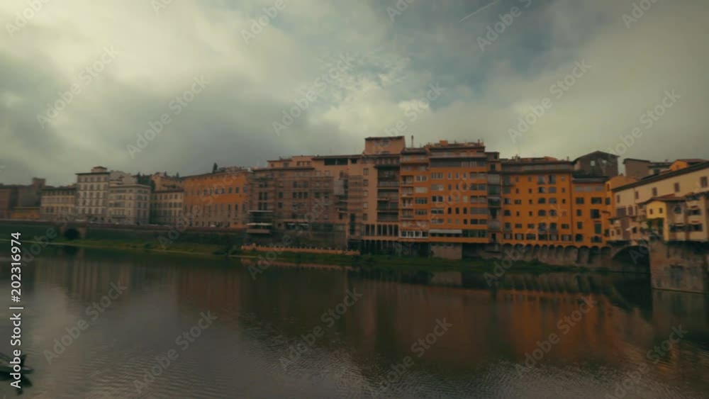 Wide angle shot panning from the Ponte Vecchio across the Arno River with the sun in the sky covered by clouds Wide angle shot panning from the Ponte Vecchio across the Arno River with the sun in the sky covered by clouds