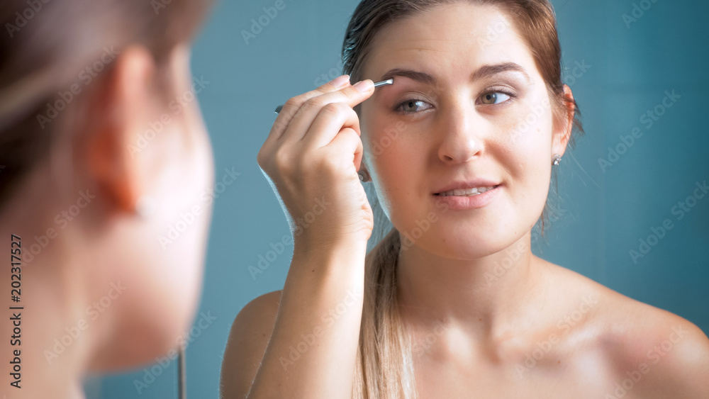 Beautiful young brunette woman plucking eyebrows with tweezers at bathroom Beautiful young brunette woman plucking eyebrows with tweezers at bathroom