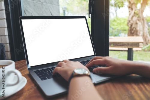 Mockup image of a woman using and typing on laptop with blank white desktop screen on wooden table in cafe