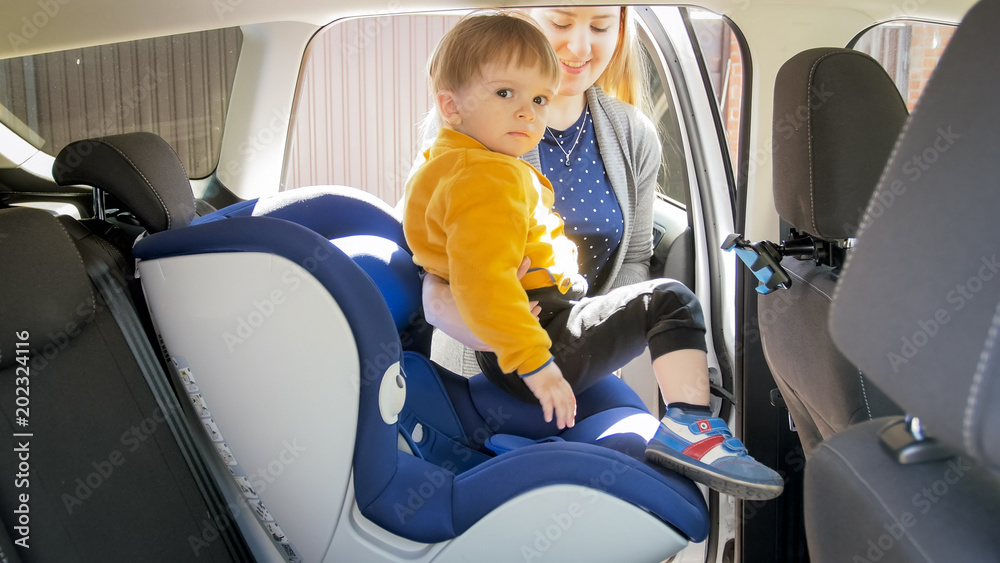 Smiling young woman seating her baby boy in car Smiling young woman seating her baby boy in car