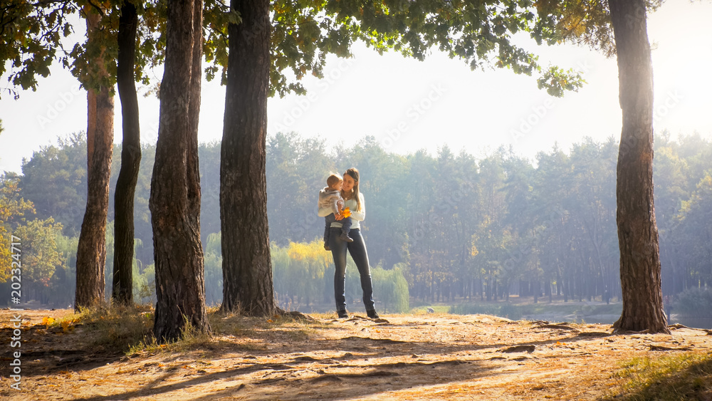 Φωτογραφία Cheerful smiling mother holding her 1 year old baby son in autumn park