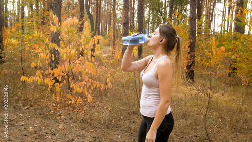 Beautiful slim woman srinking water during exercising at forest