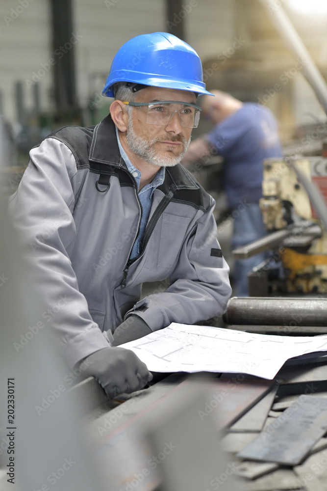 Metalworker in factory reading instructions on blueprint