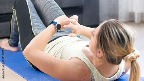 Young woman lying on fitness mat and using fitness smart watches
