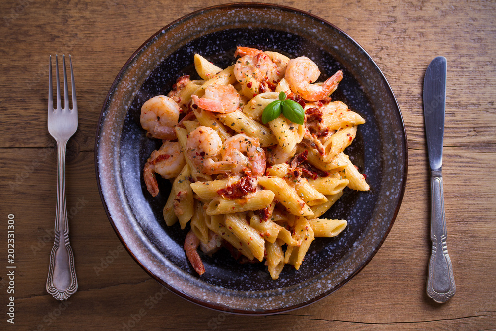 Shrimp penne with sun dried tomatoes and basil in creamy mozzarella sauce. Pasta with shrimps in bowl on wooden table. overhead, horizontal Shrimp penne with sun dried tomatoes and basil in creamy mozzarella sauce. Pasta with shrimps in bowl on wooden table. overhead, horizontal