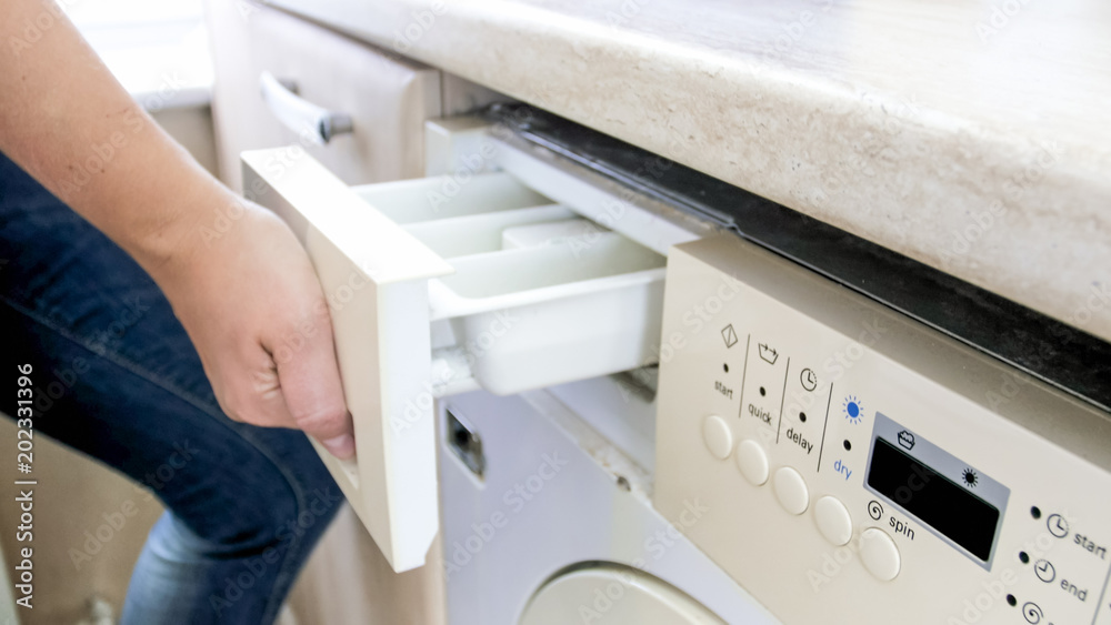 Closeup photo of young woman opens box for powder and softener on washing machine Closeup photo of young woman opens box for powder and softener on washing machine