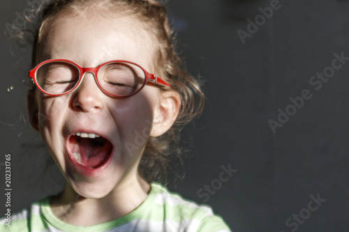 A little girl in red glasses yawns from fatigue
