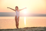 Young woman in strings swimsuit stands on the beach in sunrise