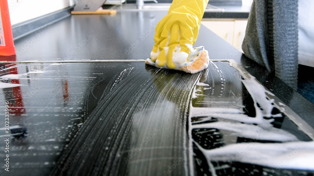 Φωτογραφία Closeup image of detergent suds on hob cleaned by young housewife in yellow glov