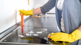 Closeup image of young woman in rubber gloves using cleaning spray while washing electric hob