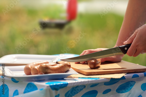 Kobieta nacina nożem kiełbasę przed grilowaniem.