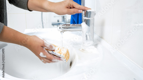 Closeup photo of young woman soaking sponge with water and detergent