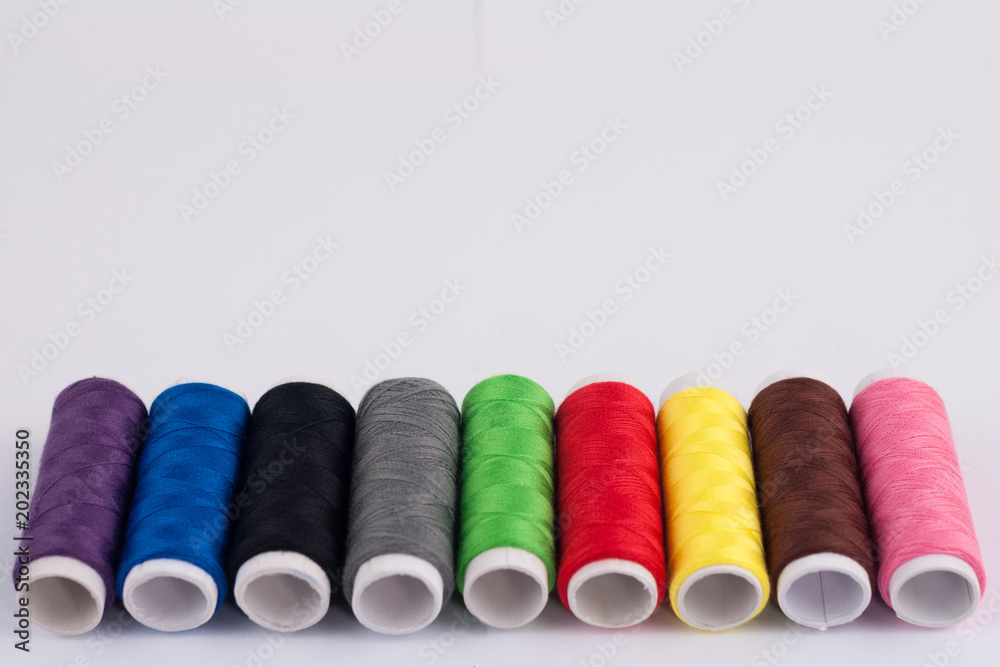 Row of bobbins of new colorful threads on white background Row of bobbins of new colorful threads on white background