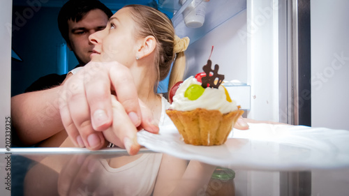 Portrait of young man stopping his wife that looking for something to eat in refrigerator photo