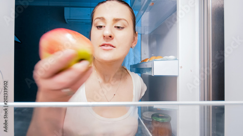 Closeup portrait of young woman taking food from refrigerator at night