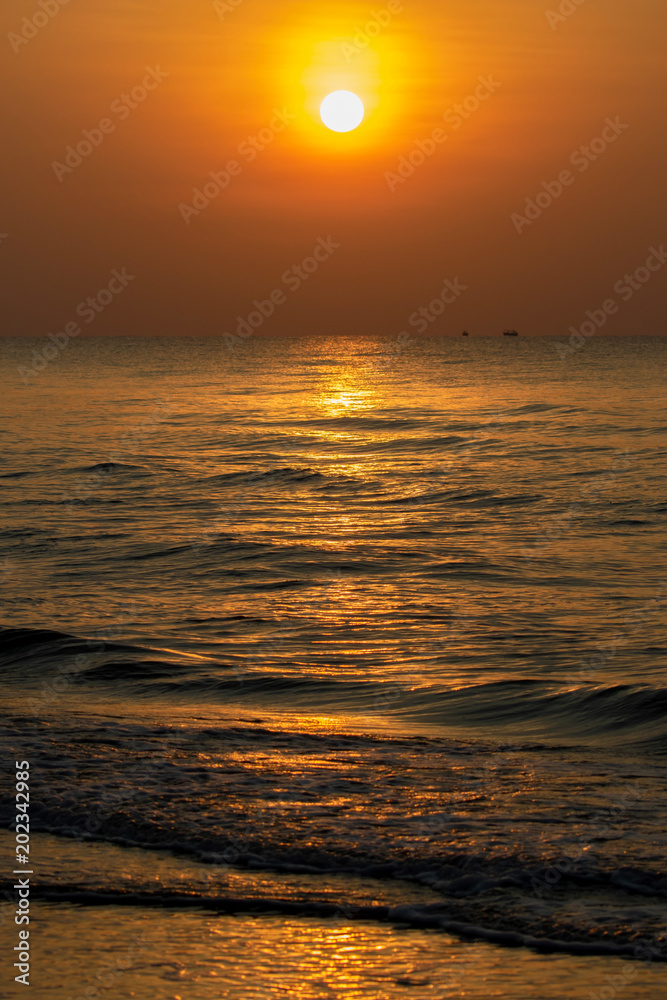 Beautiful big sunrise in the morning sky creates its stunning reflection on the sea wave surface.