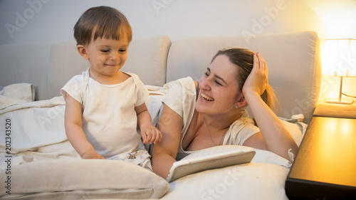 Happy cheerful mother with toddler son lying in bed at ngiht photo