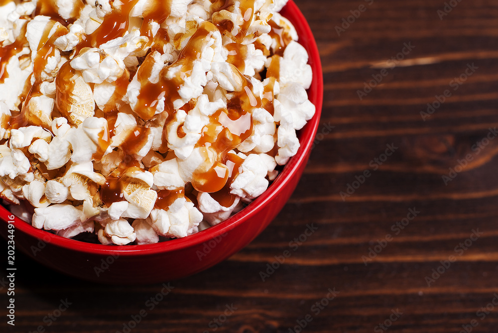 popcorn in a red bowl of poured caramel, on a dark table popcorn in a red bowl of poured caramel, on a dark table