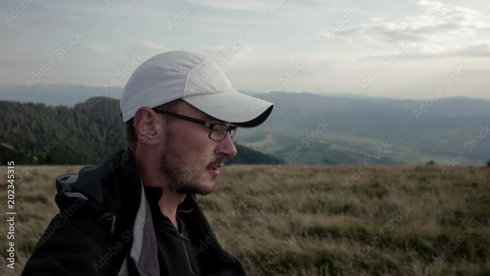 Young man in glasses and a baseball cap hiking in mountain outdoor nature scenery during summer at sunset - gimbal steadicam Young man in glasses and a baseball cap hiking in mountain outdoor nature scenery during summer at sunset - gimbal steadicam