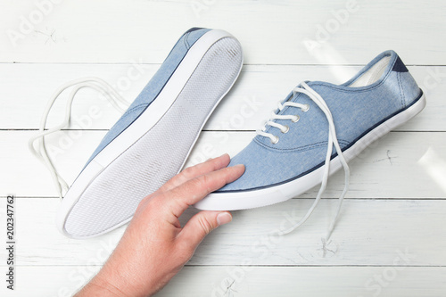 Man hand selects blue jeans sneakers on a white wooden background.