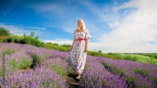 Fototapeta Naklejka Na Ścianę i Meble -  Happy blonde woman in long dress standing on lavender field