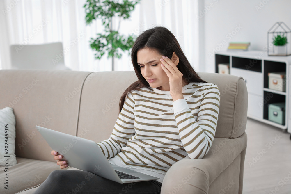 Young woman suffering from headache while sitting on sofa at home Young woman suffering from headache while sitting on sofa at home