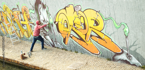Wide viewof street artist painting colorful graffiti on generic wall - Modern art concept with urban guy performing and preparing live murale with multi color aerosol spray - Retro vintage filter