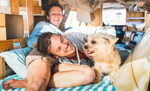 Hippie couple with funny dog traveling together on vintage minivan transport - Life inspiration concept with indie people on mini van adventure trip in relax moment - Bright warm retro filter