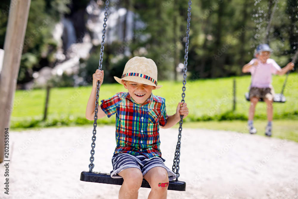 Funny kid boy having fun with chain swing on outdoor playground while being wet splashed with water Funny kid boy having fun with chain swing on outdoor playground while being wet splashed with water