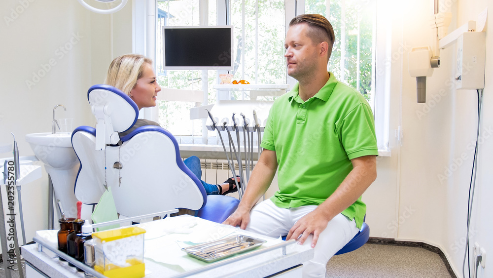 Handsome male dentist talking to his young woman patient in dentist office