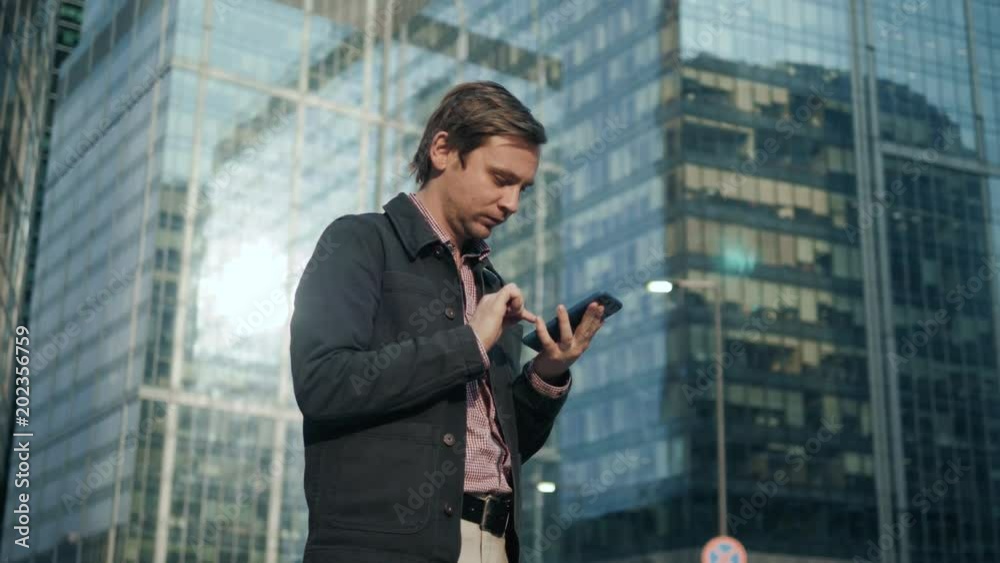 Happy smiling businessman using modern smartphone near office at early morning, successful employer to make a deal while standing near skyscraper office at night, student after university Happy smiling businessman using modern smartphone near office at early morning, successful employer to make a deal while standing near skyscraper office at night, student after university