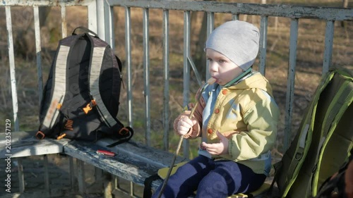 A pretty boy is eating a sausage outside. Cooked on fire bbq