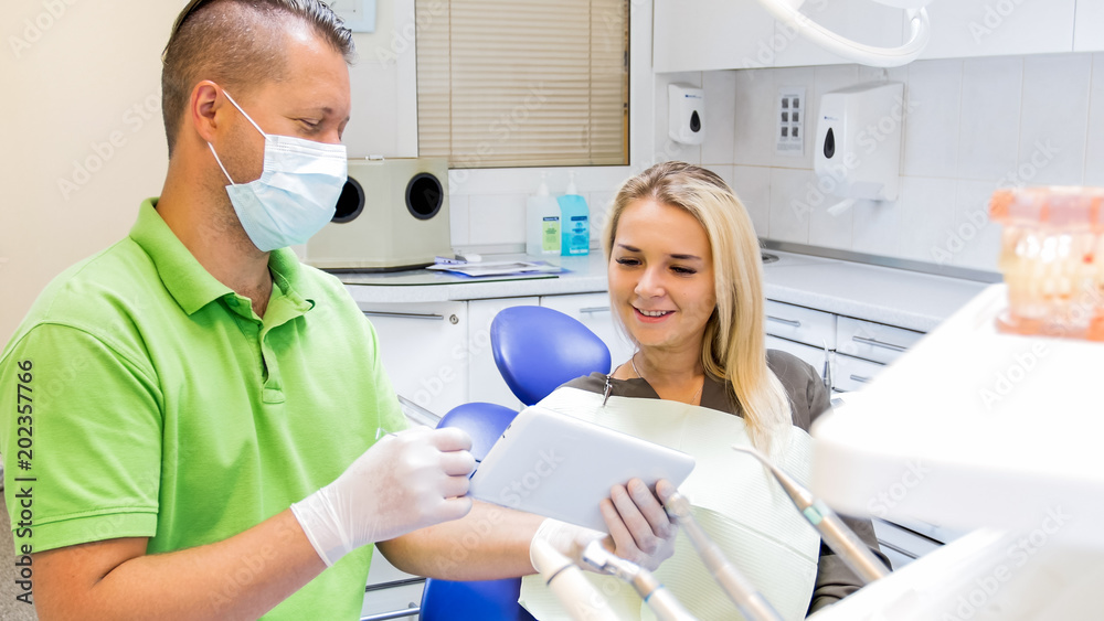 Obraz premium Portrait of beautiful blonde woman smiling after teeth treatment and looking at digital tablet
