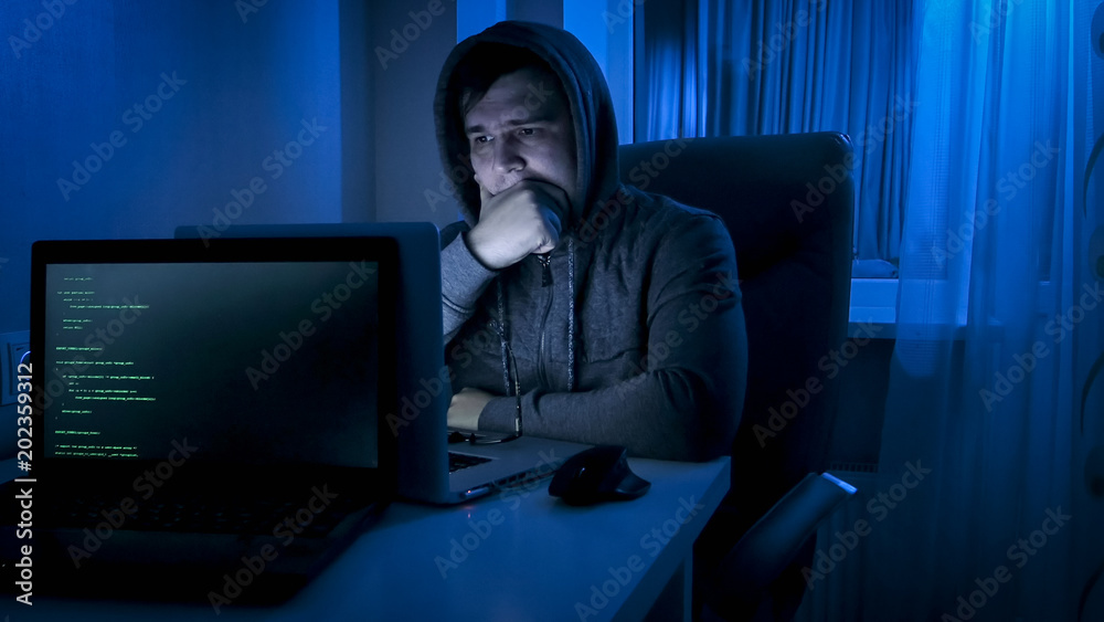 Young man in hoodie looking on laptop screeen at night Young man in hoodie looking on laptop screeen at night