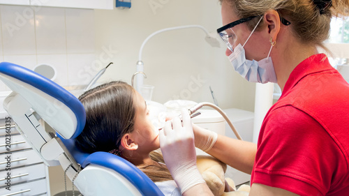 Closeup portrait of dentist treating teenage girls teeth with drill