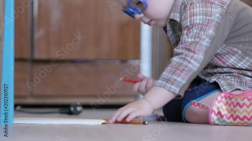 Cute boy in funny glasses draws with both hands on paper at home