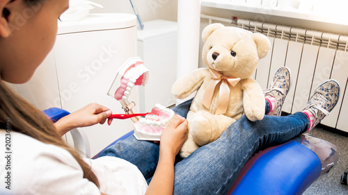 Closeup photo of little girl educating her teddy bear how to properly clean teeth