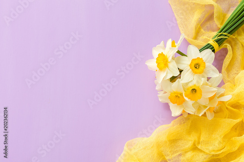 Fototapeta Naklejka Na Ścianę i Meble -  Daffodil bouquet with yellow textile decoration on violet pastel background with copy space.