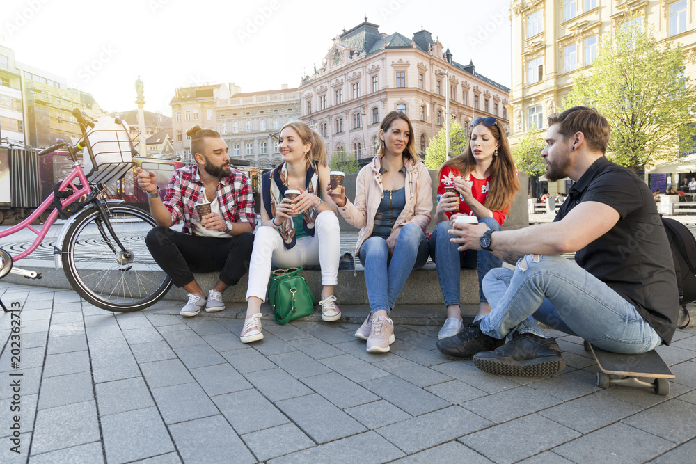 young cheerful people gathering in the city centre drinking take away coffee to go talking gossip. modern millennials communication concept