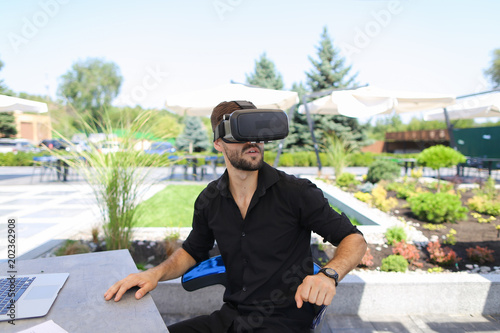 Caucasian businessman working with papers and laptop, enjoying virtual reality glasses in open air . Conceptof working online ono resort and modern technology. photo