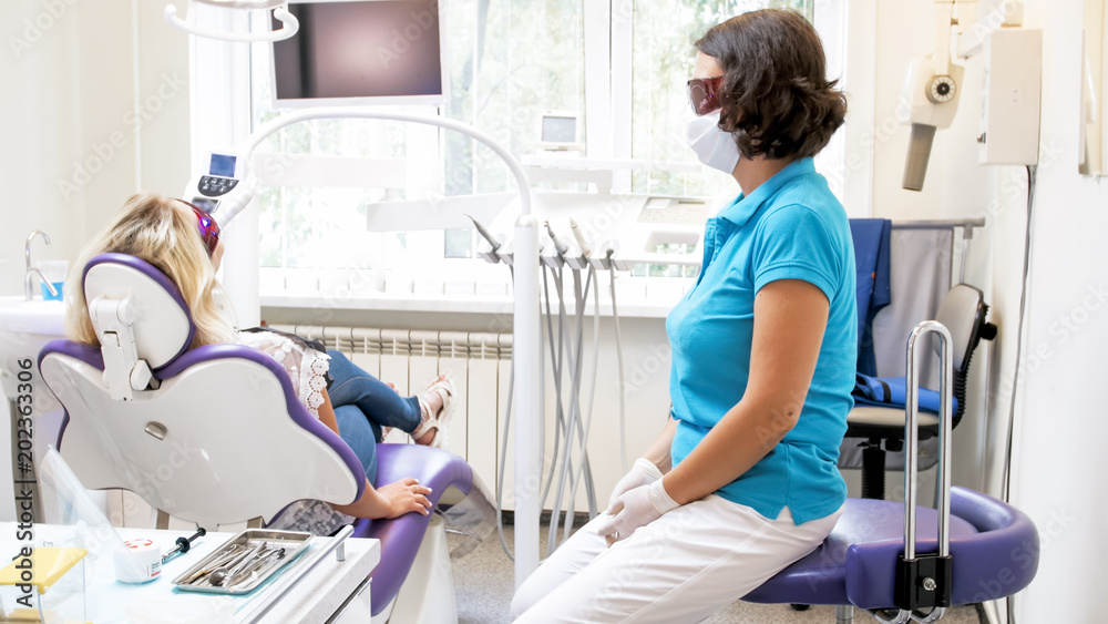 Fototapeta premium Female dentist sitting next to pateint during teeth whitening procedure