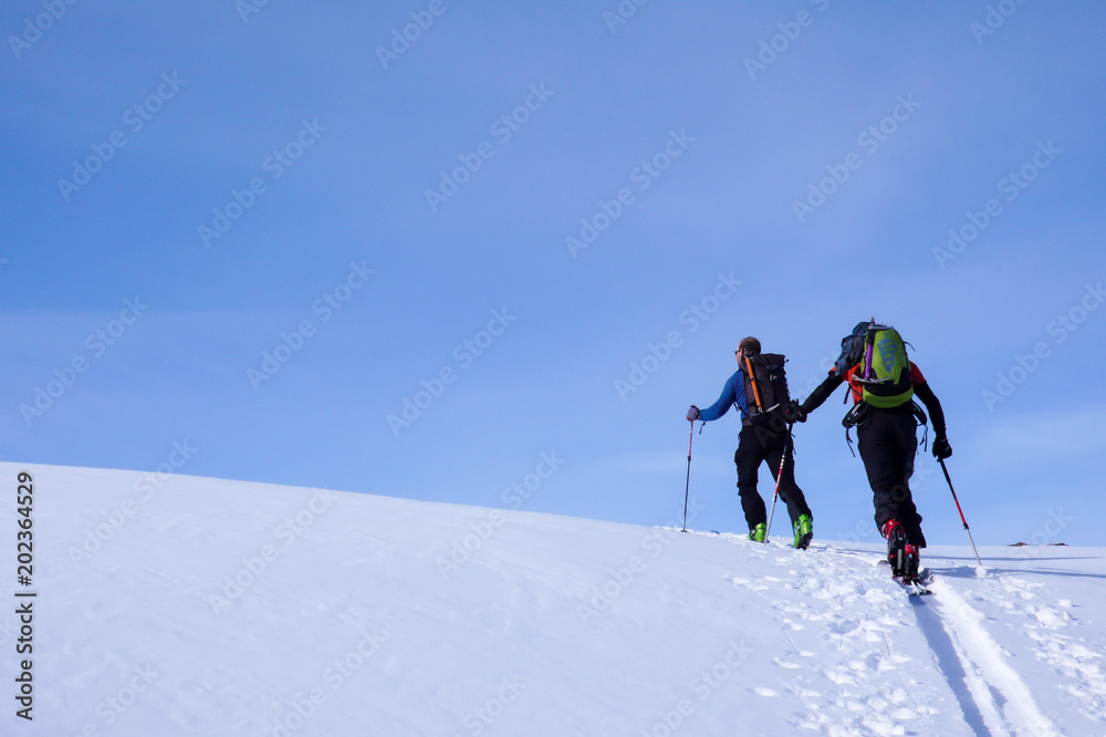 mountain guide on backcountry ski tour leading a client to the peak of a high alpine mountain