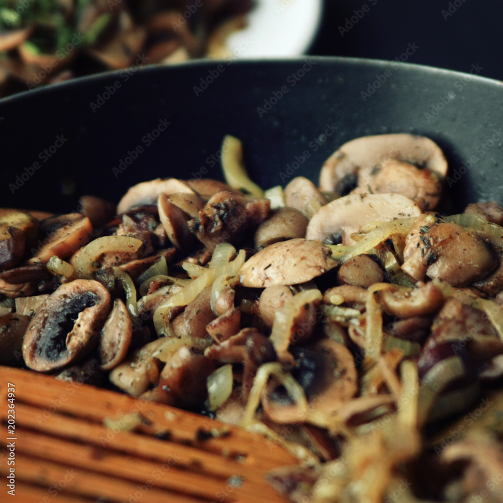 A skillet with a fried mushrooms. Vegan dish. Fried mushrooms and onion in the frying pan. European cuisine. Pan fried mushrooms. Simple vegetarian meal. Toned photo. Close up. Selective focus. A skillet with a fried mushrooms. Vegan dish. Fried mushrooms and onion in the frying pan. European cuisine. Pan fried mushrooms. Simple vegetarian meal. Toned photo. Close up. Selective focus.