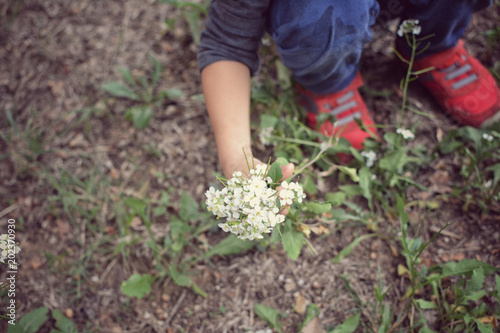 CLOSE UP CHILD SQUATTING AND HOLDING A BOUQUET OF WHITE FLOWERS