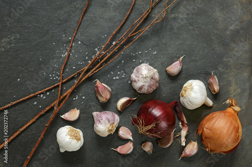 Arrangement of garlic and red onions on a natural slate table with twigs with copy space
