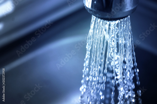 Concept water saving at home, reducing use. Water supply problems. Water tap with flowing water with spray. Selective focus photo