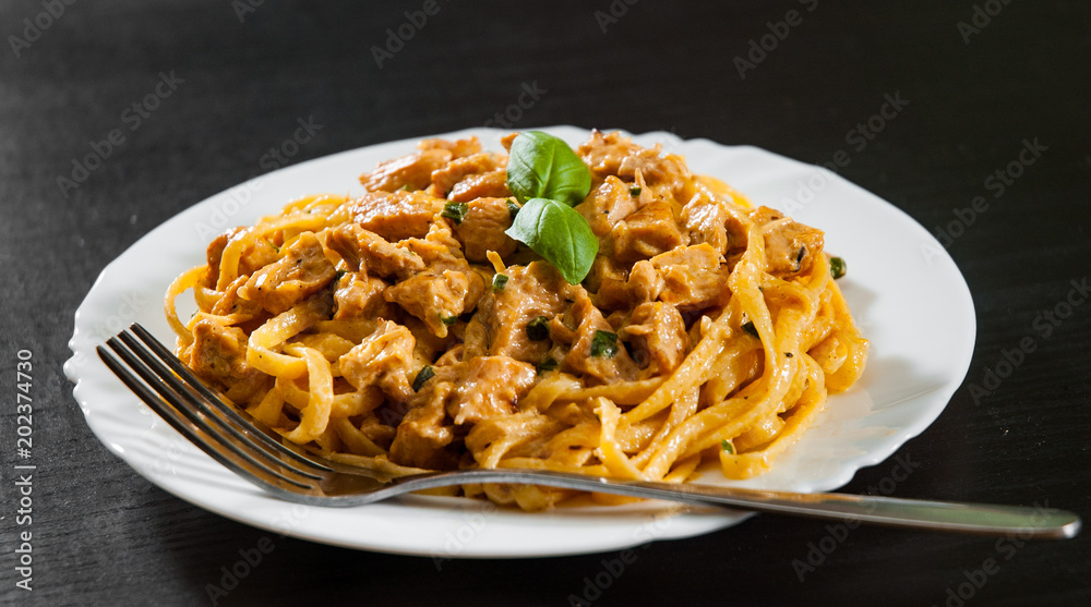 Sliced fried chicken breast meat in a creamy sauce with bavette pasta in a plate on wooden table