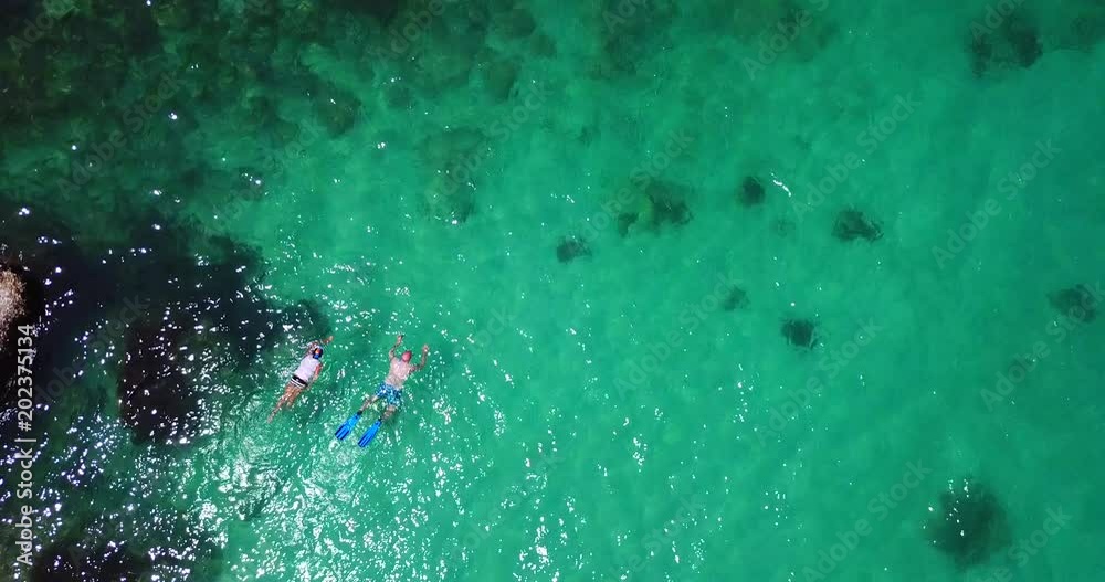 Aerial 4k: Tracking cinematic overhead movie on the people snorkeling in transparent green foaming waves against the rocky line and coral bottom Aerial 4k: Tracking cinematic overhead movie on the people snorkeling in transparent green foaming waves against the rocky line and coral bottom