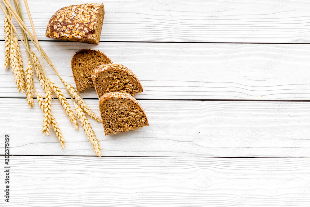 Appetizing fresh bread concept. Sliced loaf near ears of wheat on white wooden background top view copy space Appetizing fresh bread concept. Sliced loaf near ears of wheat on white wooden background top view copy space