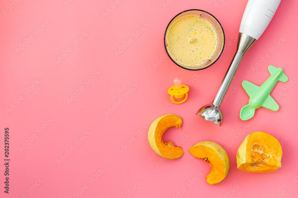 Make baby food at home. Puree with pumpkin near immersion blender, pacifier, toy on pink background top view copy space Make baby food at home. Puree with pumpkin near immersion blender, pacifier, toy on pink background top view copy space